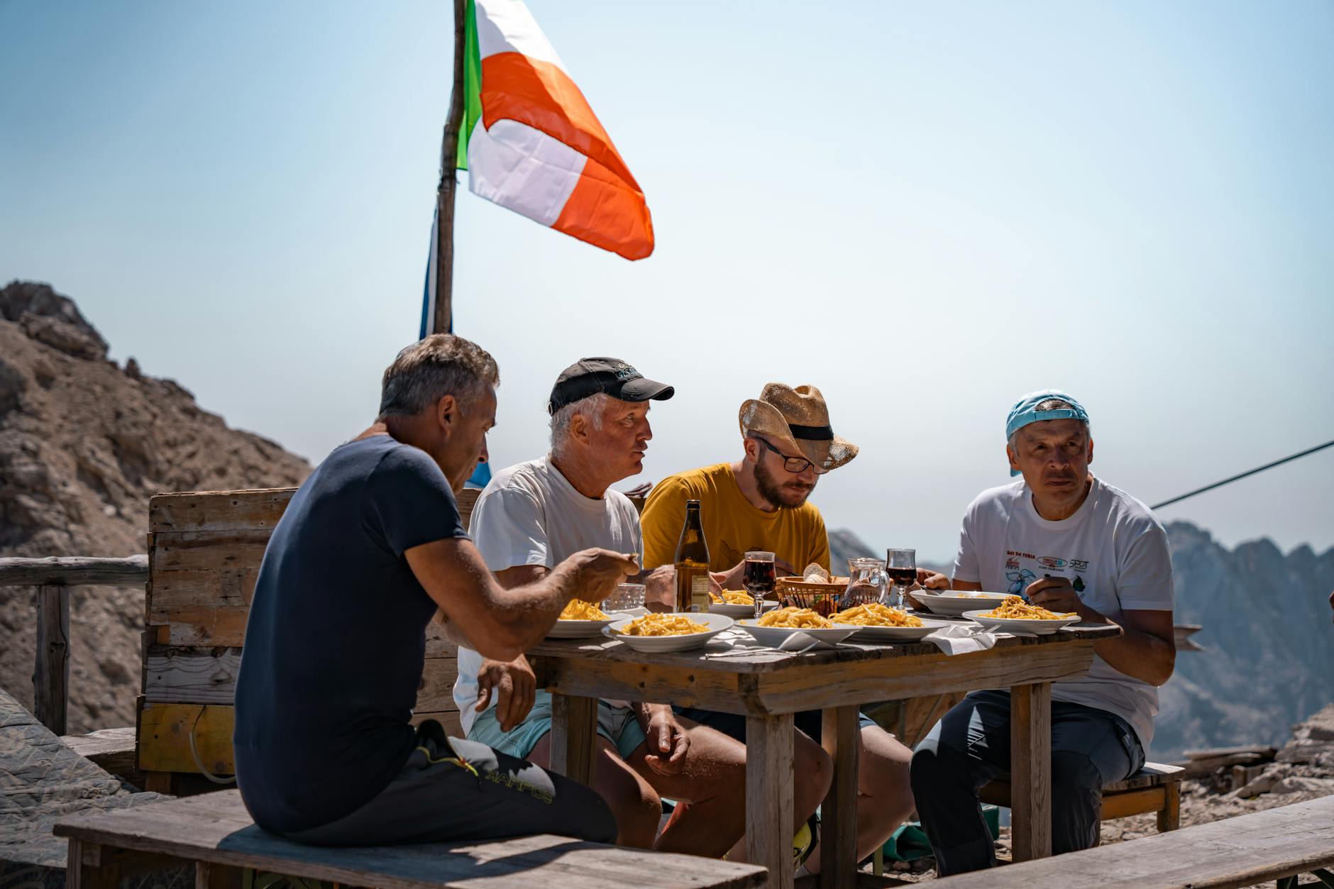 Mężczyźni jedzą makaron i piją wino w górach z włoską flagą
