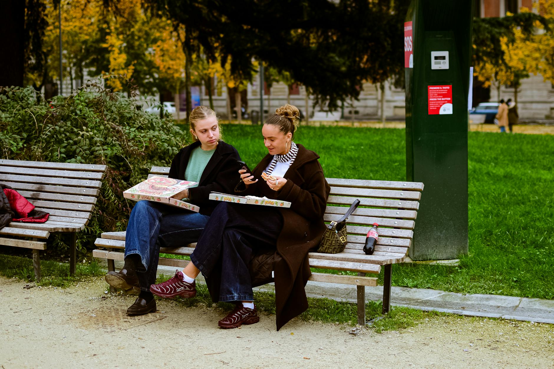 Dwie Włoszki jedzą pizzę na ławce w parku, ciesząc się chwilą