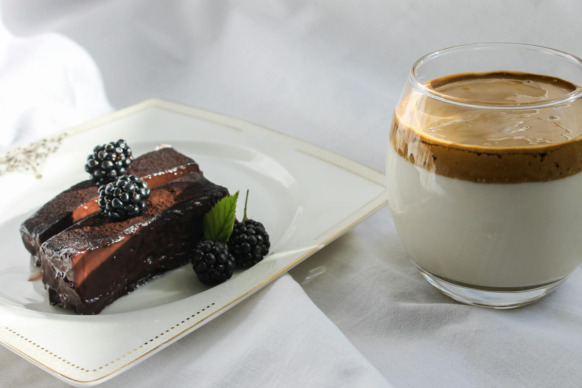 Kawa dalgona i kawałek czekoladowego ciasta z jeżynami na jasnym tle