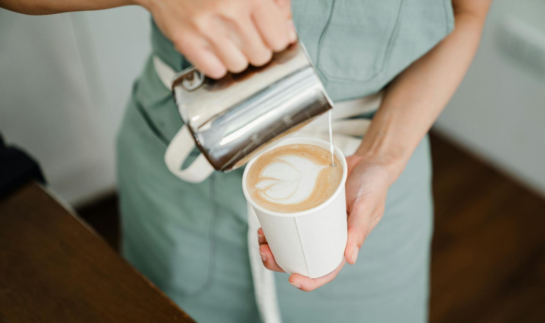 Barista w fartuchu z góry, nalewa mleko do kubka z latte macchiato