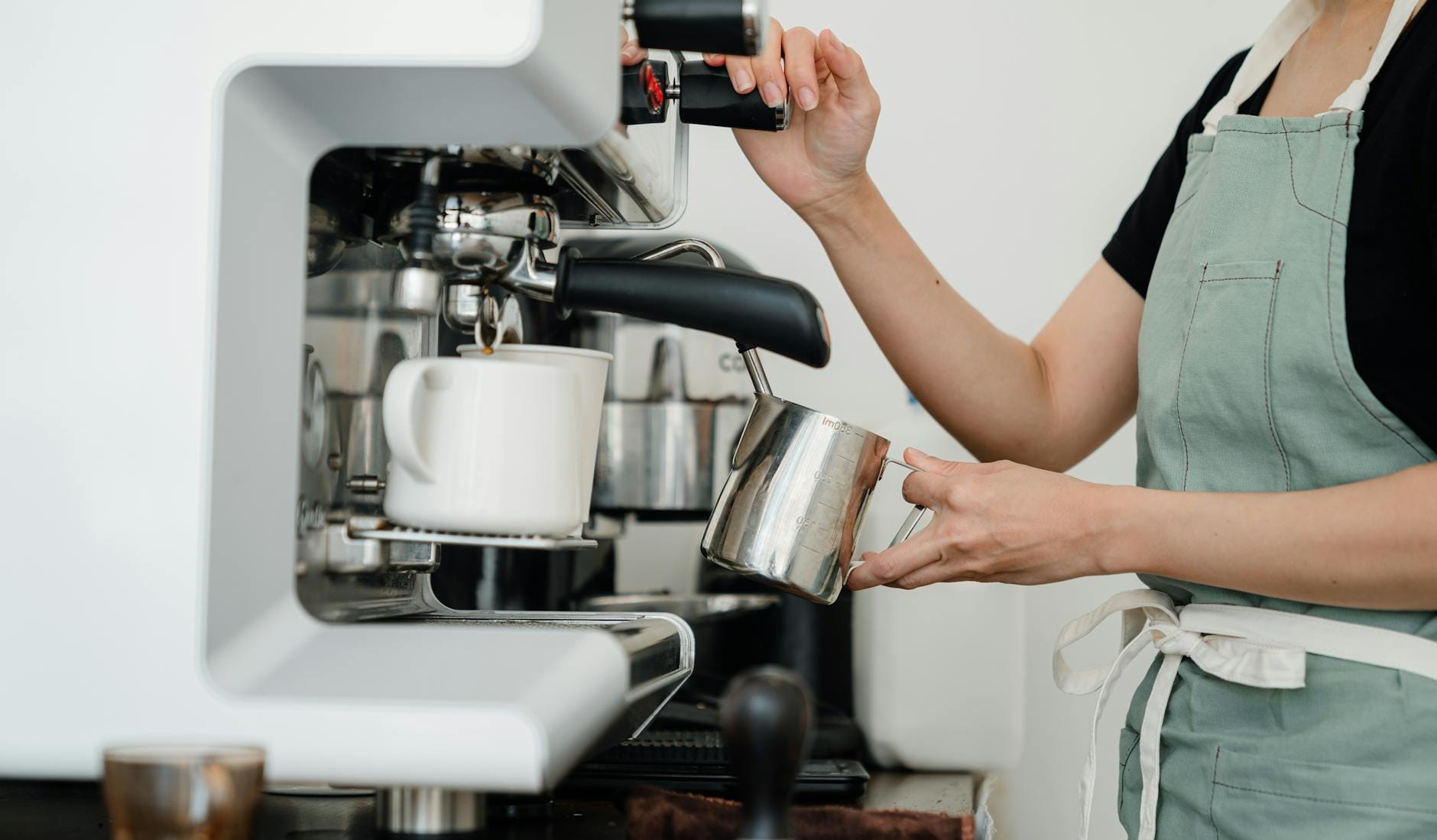 Jak zrobić latte macchiato po włosku i nie pomylić go z caffe macchiato Baristka w fartuchu spienia mleko do latte macchiato we włoskiej kawiarni