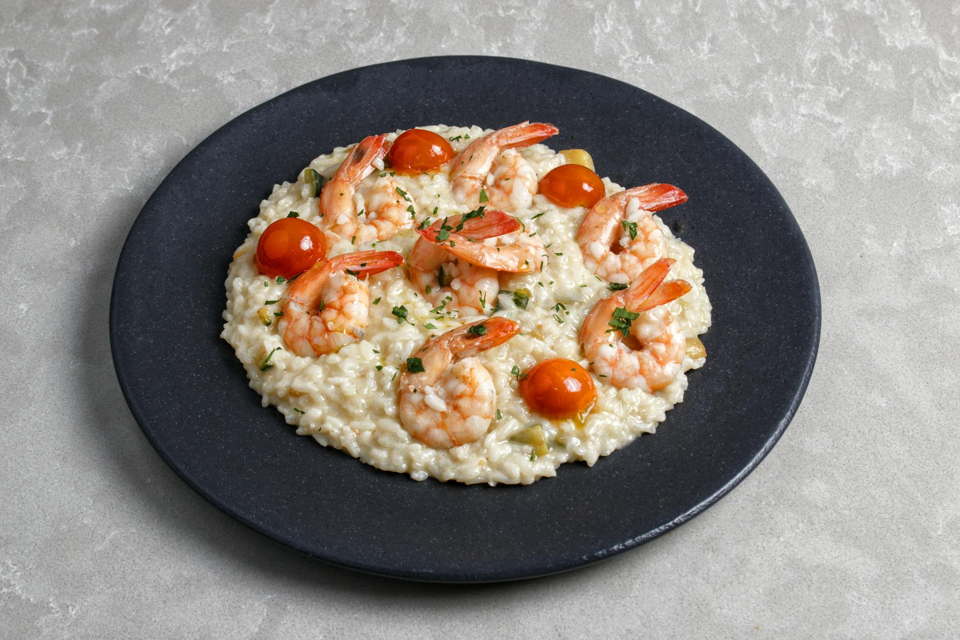 Kremowe risotto z krewetkami i pomidorkami koktajlowymi na czarnym talerzu