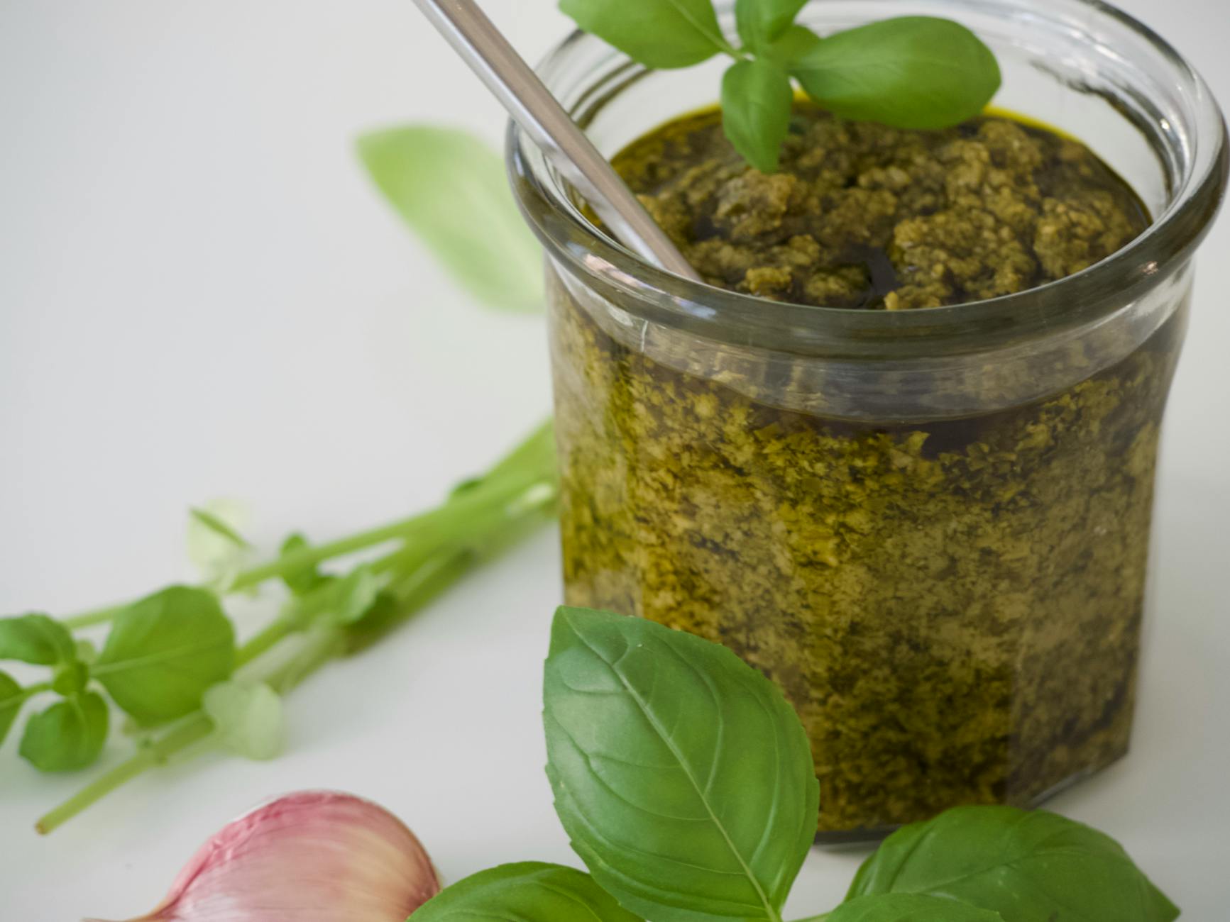 Domowy sos pesto i jego wariacje: pistacjowe, z rukolą i suszonymi pomidorami, z gotowymi pomysłami na dania Domowy sos pesto bazyliowy z czosnkiem, zbliżenie na świeże liście
