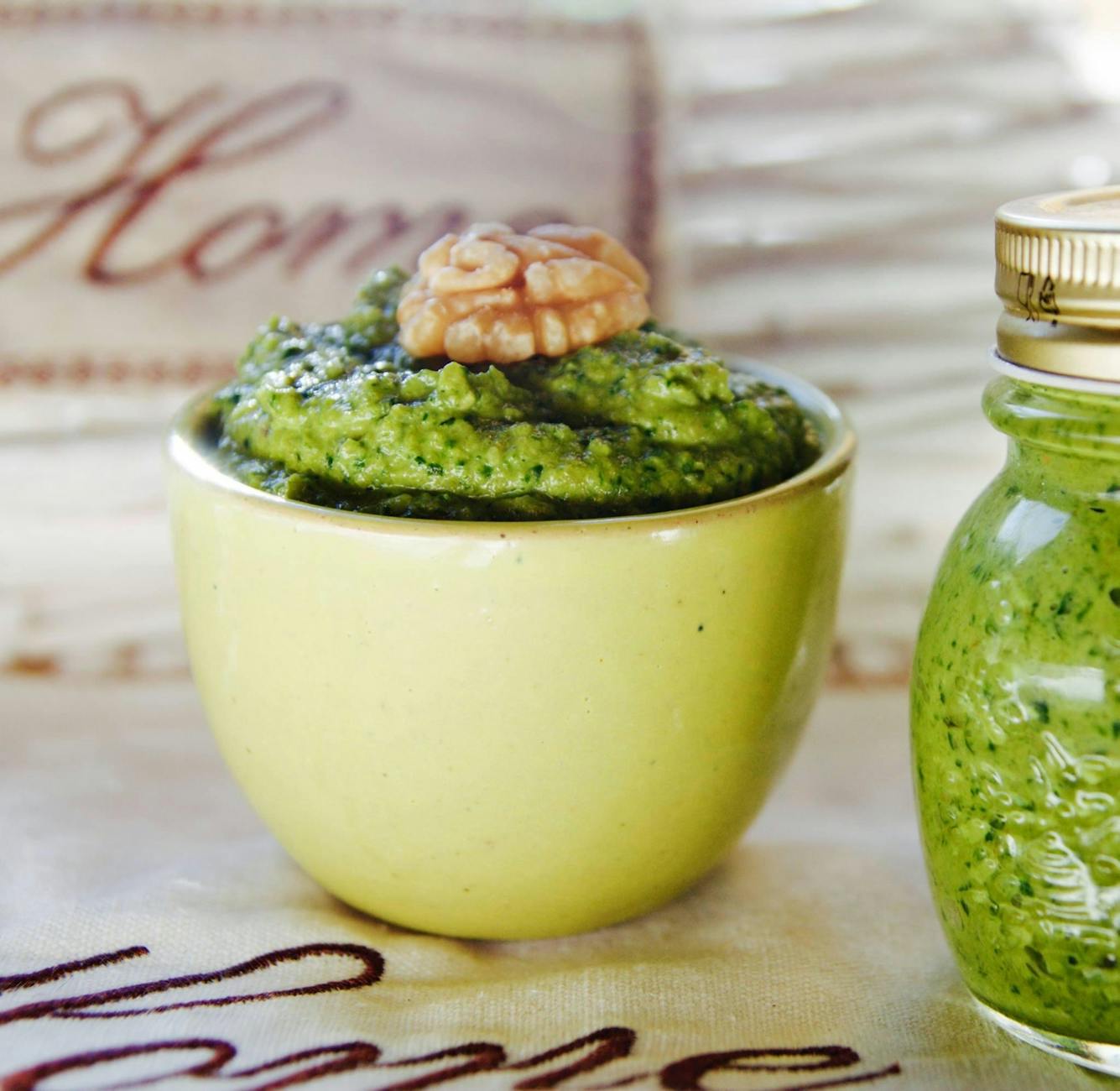 Żółta miska z domowym zielonym pesto posypanym orzechami włoskimi
