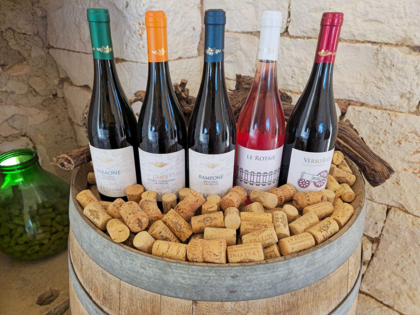 Wino na prezent: jak wybrać włoską butelkę, która ucieszy i nie zrujnuje budżetu Rustykalna beczka z różnymi butelkami wina i korkami na tle kamiennej ściany